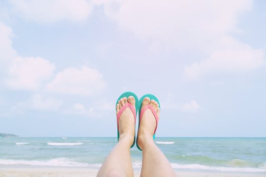 Young people wear the shoes sandals closeup show feet relaxing on beach on sand enjoying chill sun on sunny summer day. Enjoying the sea / ocean. Focus is on the feet. travel vacation holidays.