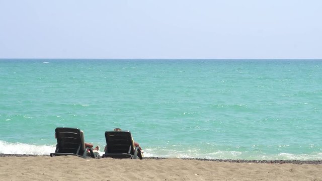 Young Couple Lying On A Lounge Chair On The Beach Watching