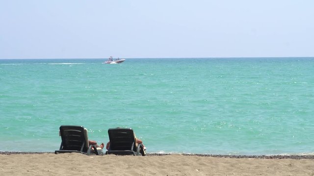 Young Couple Lying On A Lounge Chair On The Beach Watching