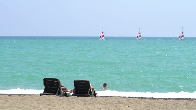 Young Couple Lying On A Lounge Chair On The Beach Watching