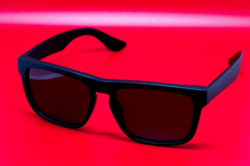 Fashion sunglasses isolated on red background, black plastic.