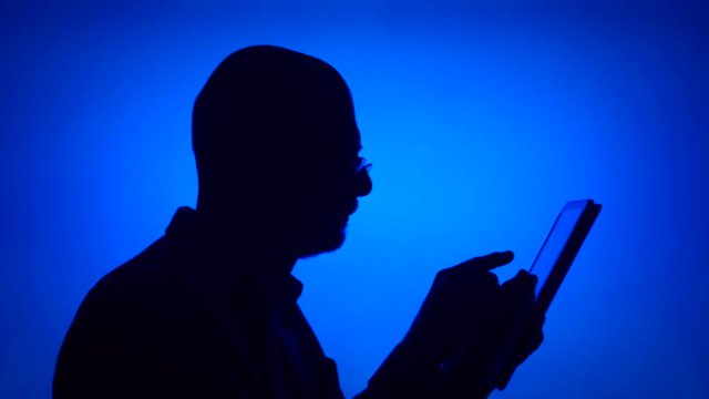 Silhouette of senior man use tablet on blue background. Male's face in profile browse, read, chat online with family and friends on computer. Black contur shadow of grandfather's half-face