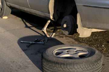 Replacing the rear wheel of the car. The car is mounted on the Jack. On asphalt lie screws, tool and wheel.