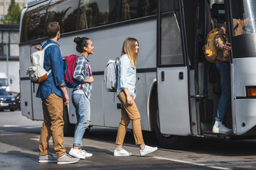young smiling tourists with rucksacks walking into travel bus at city street © LIGHTFIELD STUDIOS