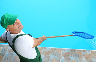 Male worker cleaning outdoor pool with scoop net