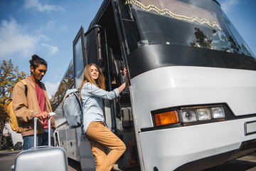 Naklejka premium selective focus of mixed race man standing with wheeled bag while his girlfriend walking into travel bus at street
