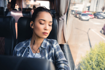 young asian woman sleeping and listening music in earphones during trip on travel bus