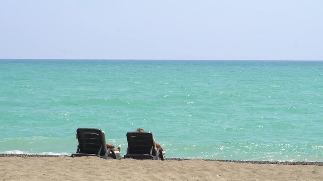 Young Couple Lying On A Lounge Chair On The Beach Watching