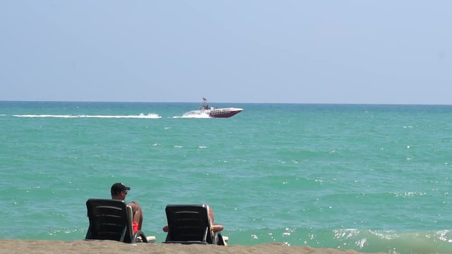 Young Couple Lying On A Lounge Chair On The Beach Watching