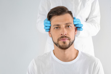 Doctor examining mature man face before cosmetic surgery on white background