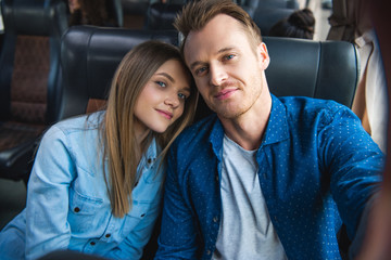 cheerful man taking selfie with young girlfriend during trip on travel bus