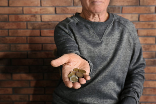 Poor elderly man begging for money near brick wall, focus on hand