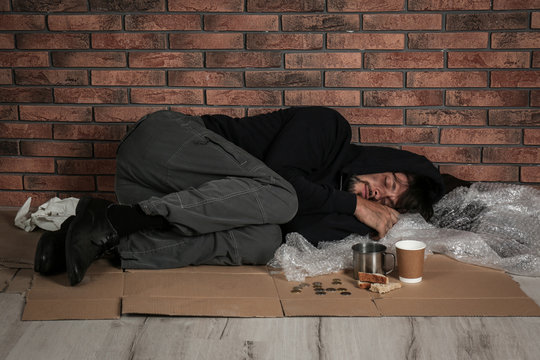 Poor man sleeping on floor near brick wall