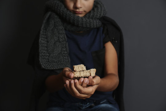 Poor boy with pieces of bread on dark background, focus on hands