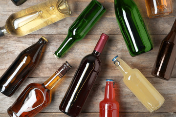 Bottles with different alcoholic drinks on wooden background, flat lay