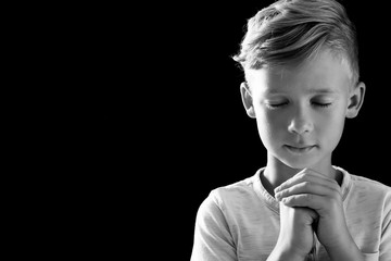 Little boy with hands clasped together for prayer on dark background, black and white effect. Space for text