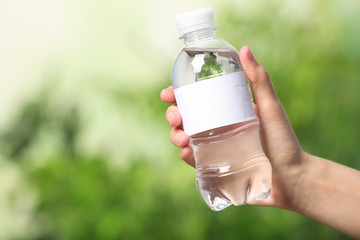 Woman holding bottle of water on blurred background. Space for text