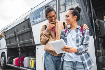 young interracial couple of tourists standing with digital tablet near travel bus at street