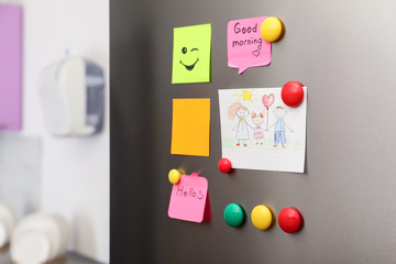 Paper sheets, child's drawing and magnets on refrigerator door indoors