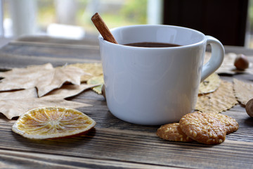 Hot chocolate with cinnamon stick in cup leaves nuts cookies dried oranges on wooden table Autumn hot drink Autumn concept