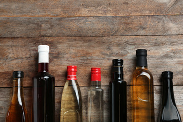 Bottles with different kinds of vinegar and space for text on wooden background, flat lay