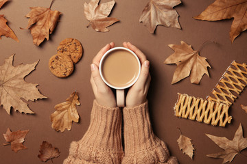 Woman in autumn sweater holding hot cozy drink on color background, top view