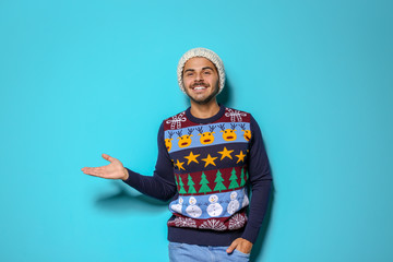 Young man in Christmas sweater and knitted hat on color background