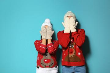 Young couple in Christmas sweaters and knitted hats on color background