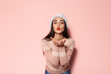 Young woman in warm sweater and knitted hat on color background. Celebrating Christmas