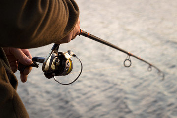 Fishing rod, reel, fisherman fishing spinning on canal at sunset