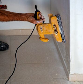 Worker with an orbital sander smoothes a wall