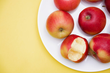 several whole red apples and one bitten in a plate on a yellow background of autumn composition and concept