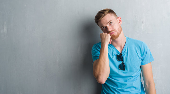 Young redhead man over grey grunge wall wearing casual outfit thinking looking tired and bored with depression problems with crossed arms.