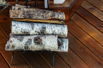 Birch firewood for the fireplace on wooden floor near the door at forest house