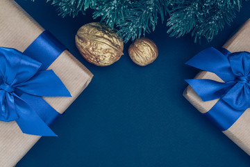 Gifts in paper with blue ribbon and bow-knots with gold nuts and branches of spruce on a dark-blue background. - obrazy, fototapety, plakaty
