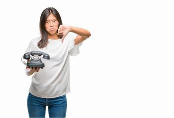 Young asian woman holding vintagera telephone over isolated background with angry face, negative sign showing dislike with thumbs down, rejection concept