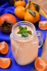 Fruit smoothie in a glass jar topped with mint surrounded by persimmon and mandarins