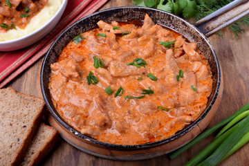 Pieces of meat stewed in tomato and sour cream sauce in the frying pan