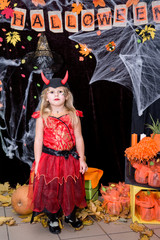 A child, a little girl in the shape of a witch on a broomstick, poses against the backdrop of scenery of cobwebs, pumpkins and autumn leaves on a Halloween holiday.