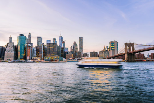 Outdooors view on NYC New York City Brooklyn Bridge Park by east river, cityscape skyline at sunset, dusk, twilight, skyscrapers, buildings, waves, blur, blurry tour boat - Powered by Adobe