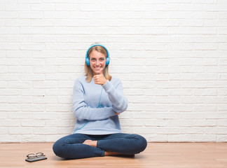 Beautiful young woman sitting on the floor listening music wearing headphones at home happy with big smile doing ok sign, thumb up with fingers, excellent sign