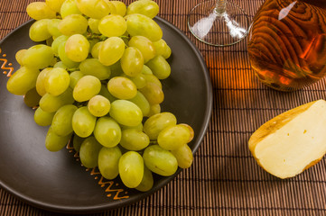 large brush of green grapes in a ceramic plate, a decanter and a glass of wine and cheese
