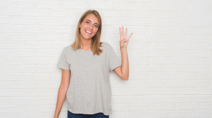 Beautiful young woman over white brick wall showing and pointing up with fingers number four while smiling confident and happy.