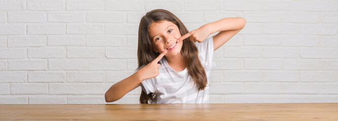 Young hispanic kid sitting on the table at home smiling confident showing and pointing with fingers teeth and mouth. Health concept.