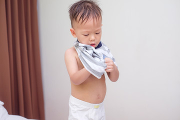 Cute little Asian 2 years old toddler boy child in bed concentrate on putting on his striped T Shirt, Encourage Self-Help Skills in Children, The growth of independence in young child concept