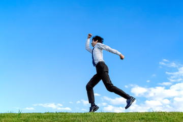 青空をバックにジャンプするYシャツ姿の若いビジネスマン1人。元気・パワー・喜び・挑戦イメージ