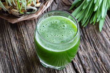 A glass of barley grass juice with young barley grass in the background