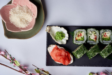 Green sushi set with chuka served on black clay plate with soy sauce and chopsticks, top view. Delicious traditional Japanese food, sushi restaurant concept