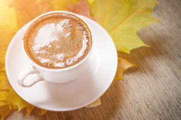 Autumn leaves and coffee cup over wood background with copy space