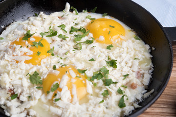 Fried eggs in a frying pan with cheese and aromatic herbs